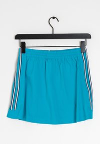 Blå sportkjol med elastisk midja och sidostråk i vitt och marinblått, hängande på en svart galge mot vit bakgrund.