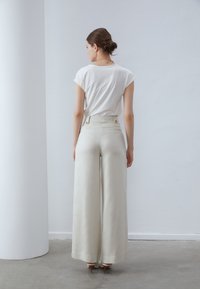 Crème brede pantalon met een hoge taille en zijzakken, gecombineerd met een nauwsluitend wit t-shirt. Gladde textuur en minimalistisch ontwerp.