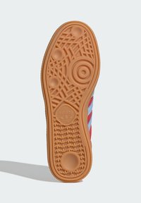 Podošva oranžovej tenisky Adidas zobrazuje kruhové, mriežkové a logo vzory, pričom svetlo modrá a červená horná časť sú viditeľné na strane.