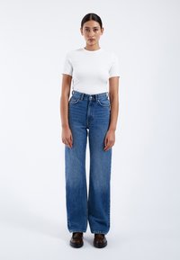 Camisa blanca de manga corta con escote redondo, combinada con unos pantalones vaqueros de cintura alta y pernera amplia en azul, y zapatos de plataforma marrones. Diseño sencillo y casual.