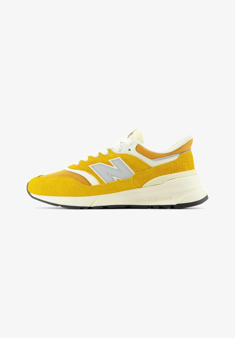 Gul mocka och mesh sneaker med vita accenter och en tjock sula. Har en framträdande grå "N"-logotyp på sidan.