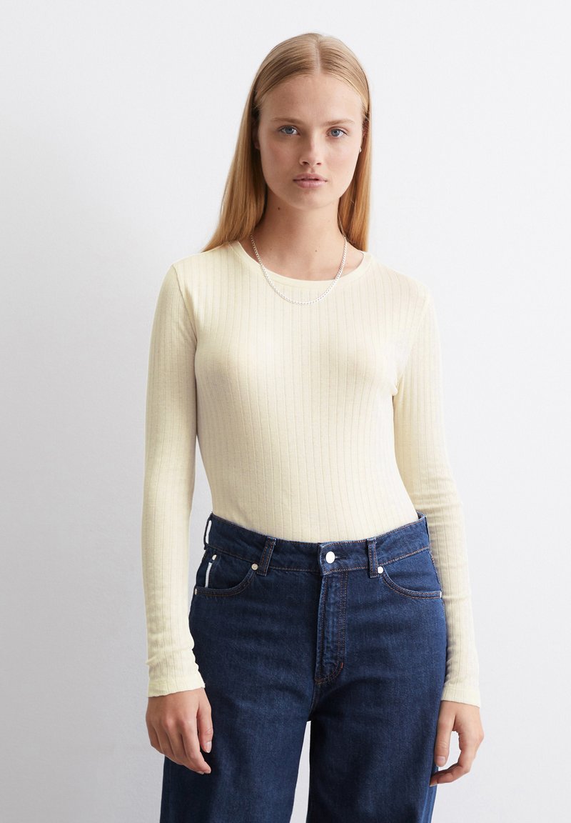 Geribbelde langemouwen top in lichtgeel, aansluitend ontwerp. Gecombineerd met hoge taille donkerblauwe denim jeans, met klassieke vijf-pocket stijl.