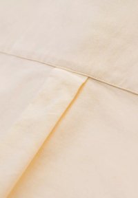 Gros plan sur un tissu beige montrant un pli plié et un détail de couture cousue.