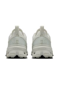 Light gray athletic shoes with textured fabric, reinforced heel, and distinctive cushioning, featuring a pull tab on the back.