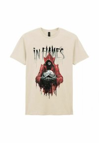 Beige cotton t-shirt featuring a black and red graphic of a cloaked figure holding a skull with white accents, and the text "IN FLAMES" above.