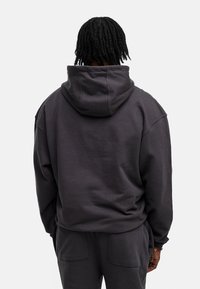 Dunkelgrauer, übergroßer Kapuzenpullover mit großer Kapuze, überschnittenen Schultern und strukturiertem Stoff. Die Rückseite ist glatt und hat keine sichtbaren Logos oder Muster.