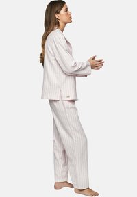 Ensemble de pyjama rose clair avec de fines rayures blanches, comprenant une veste à boutons et un pantalon ampla. Le matériau semble doux ; aucun motif ou accent noté.