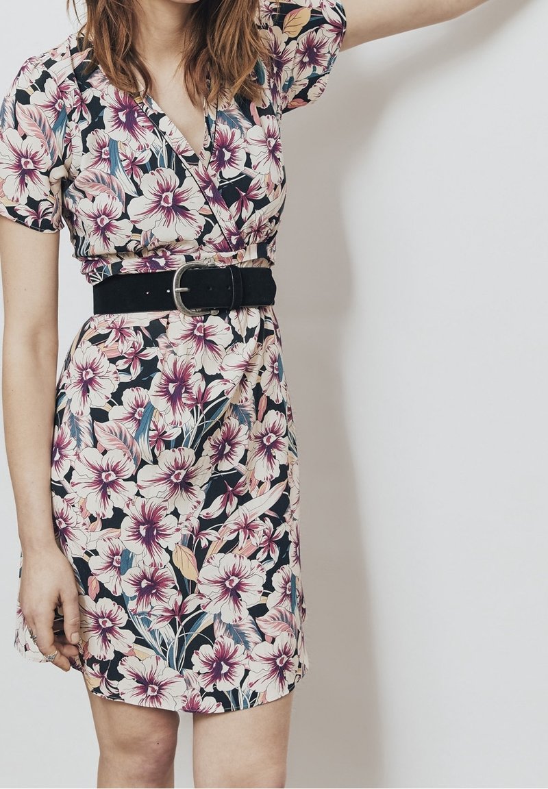 Vestido floral con un fondo negro y grandes flores rosas y blancas. Diseño envolvente con mangas cortas y un cinturón negro en la cintura.