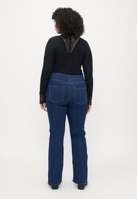 T-shirt preta de mangas longas com detalhes em renda nas costas, combinada com jeans flare de tom azul escuro, apresentando bolsos traseiros e uma cintura de altura média.