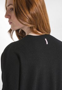 Maglione nero lavorato a maglia con scollatura rotonda e tessuto testurizzato. Piccolo etichetta rosa sul retro del collo. Design semplice e dal taglio rilassato.