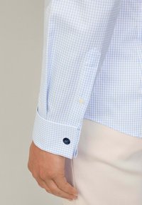 Blauw-wit geruit overhemd met een knoopmanchet, voorzien van een witte knoop en een donkerblauwe accentknoop. Glad stoffen structuur.