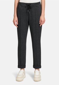 Graue, zulaufende Hose aus strukturiertem Stoff, mit verstellbarem Kordelzug in der Taille und hochgekrempelten Bündchen, kombiniert mit hellen Sneakern.