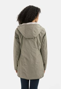 Olive green jacket with a hood, featuring a textured lining, long sleeves, and a curved hem. Made from lightweight, water-resistant material.