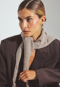 Bufanda de lana gris drapeada alrededor del cuello, textura suave, combinada con un blazer oscuro, diseño minimalista y líneas limpias, entorno de luz natural.