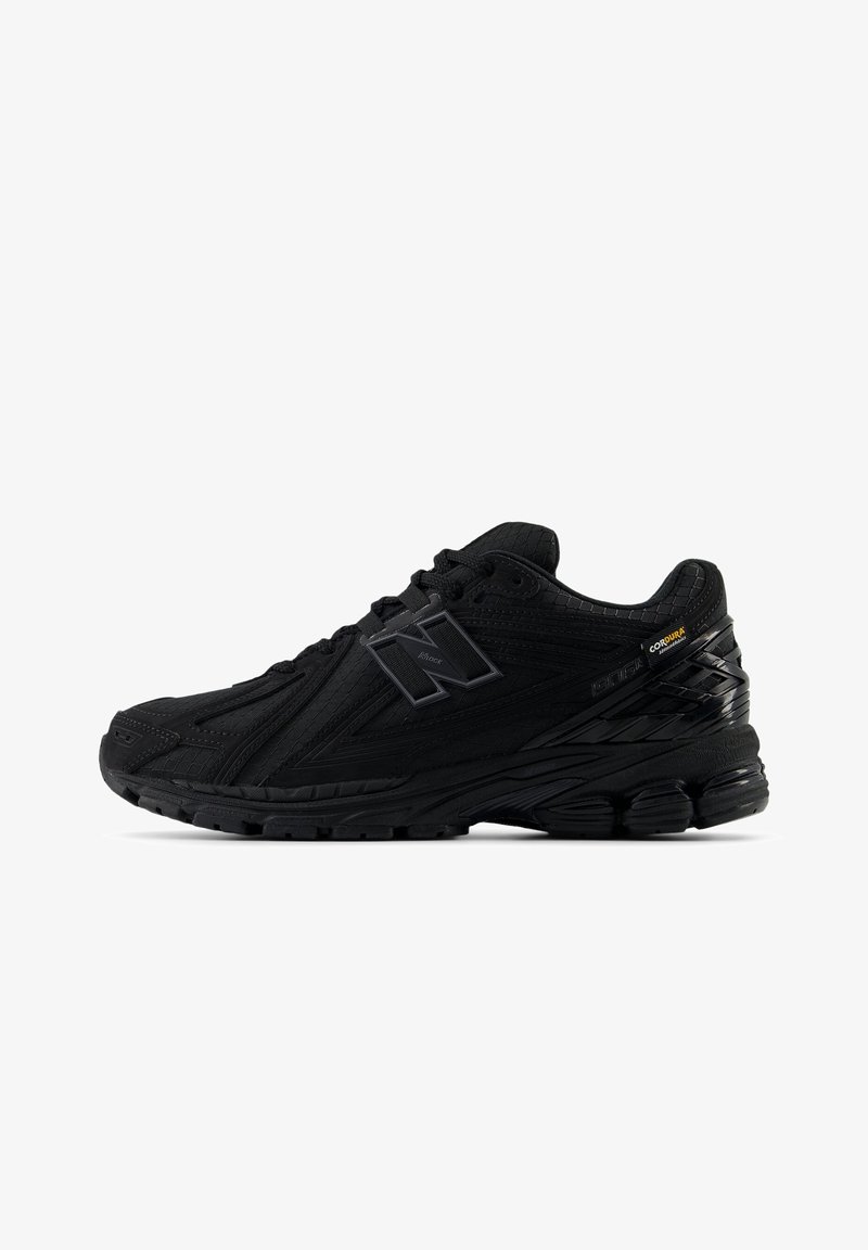 Baskets de sport noires avec dessus texturé, semelle matelassée, lacets, et marque en tissu Cordura sur le côté.