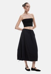 Zwarte crop top met geribbelde textuur, gecombineerd met een vloeiende zwarte midi-rok met een elastische tailleband en een geplooide zoom.