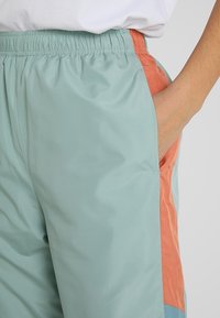 Lätta, mintgröna shorts med elastisk linning, med sidofickor och orangea detaljer längs sidorna. Slät textur.