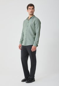Light green button-up shirt in a linen blend, featuring a collar, long sleeves, and an even texture, paired with black trousers and shoes.