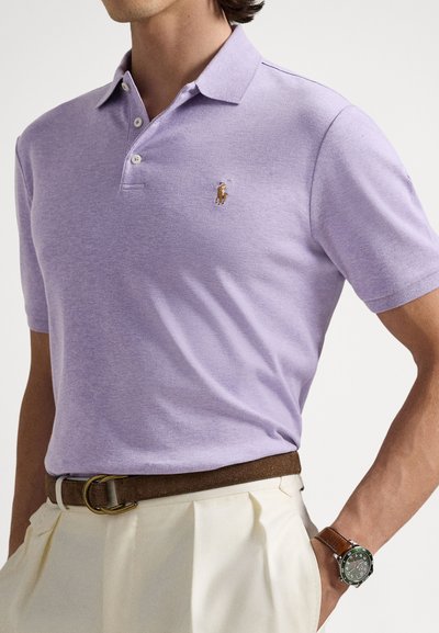 Πόλο μπλουζάκι σε χρώμα λεβάντας με τρεις κουμπότρυπες, κοντά μανίκια και ένα μικρό κεντητό λογότυπο στο στήθος. Καφέ δερμάτινη ζώνη.