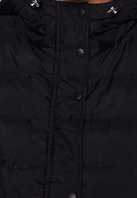 Czarna kurtka puchowa z pikowanym wzorem, zatrzaskami oraz zebranym kapturem ze sznurkiem. Gładka, błyszcząca tekstura zewnętrzna.