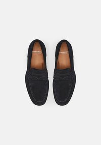 Zilīgi zilo zamšādas loafers ar gludu tekstūru, kontrastējošām šuvēm un noapaļotu purngalu. Iekšpusē ir brūnas ādas oderes.