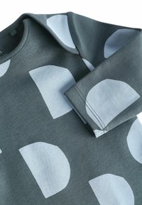 Zelena sweatshirt z svetlo modrimi okroglimi vzorci. Ima okroglo ovratnico in dolge rokave. Narejena je iz teksturiranega bombažnega materiala.