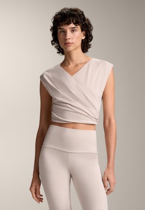 Cream-colored, wrap-style top with short sleeves, paired with matching high-waisted leggings. Smooth texture, minimalist design, fitted silhouette.