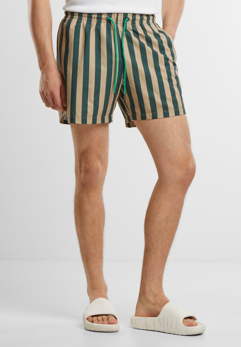 Gestreifte Badeshorts in Beige und Dunkelgrün. Hergestellt aus leichtem Material, mit einem elastischen Bund und einer grünen Kordel.