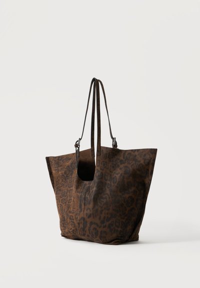 Grand sac cabas marron avec un motif léopard foncé et deux fines bretelles sur un fond clair uni.