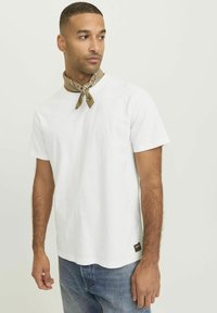 White cotton t-shirt with a round neckline, short sleeves, paired with a patterned brown scarf tied around the neck. Denim jeans visible.