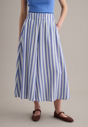 Donna che indossa una gonna midi a righe verticali blu e bianco con tasche, un top blu senza maniche e ballerine marroni Mary Jane.