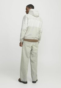 Lysegrå vindjakke med en hvid vandret stribe, elastisk talje og hætte; parret med løstsiddende lyse denim jeans.