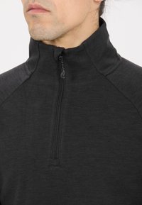 Schwarzer Halbreißverschluss-Pullover aus einem weichen, strukturierten Stoff mit hohem Kragen und kontrastierenden Schulterdetails. Reißverschluss am Hals.