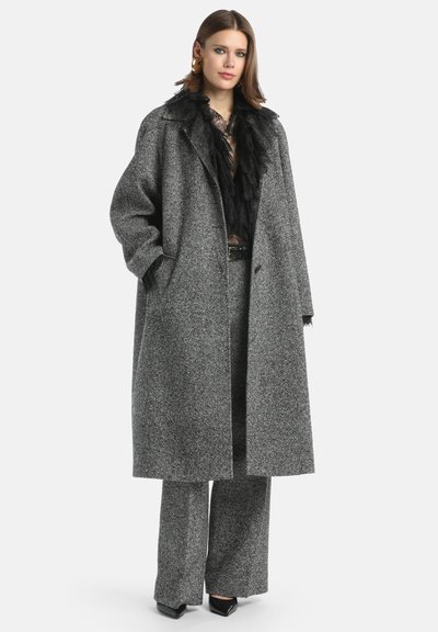 Preveliki sivi vuneni kaput s teksturiranim izgledom. Ima rever kragnu i velike džepove. Uparen s širokim sivim hlačama i crnim štiklama.