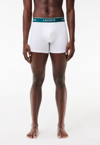 White boxer briefs with a green Lacoste waistband. Made of soft fabric, featuring a fitted design and a contour pouch for comfort.