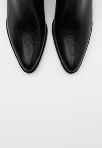 Paire de bottes en cuir noir à bout pointu avec une couture décorative subtile sur le dessus, vue de dessus sur un fond blanc.