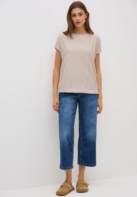 Camiseta beige de manga corta con un patrón de diamante texturizado, combinada con vaqueros cortos azules y zapatos de lona marrón claro.