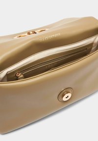 Beżowa torba z faux skóry o gładkiej fakturze, z złotymi akcentami i magnetycznym zapięciem; wnętrze zawiera kieszeń zamykaną na zamek oraz detal z logo.