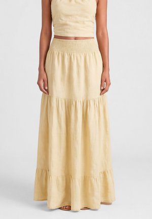 Kobieta nosząca jasnobeżową, warstwową spódnicę maxi z szerokim elastycznym pasem i dopasowanym bezrękawnym krótkim topem.