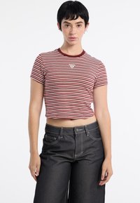 Czerwono-biały, pasiasty crop top z krótkim rękawem i okrągłym dekoltem, ozdobiony trójkątnym logo marki. Połączony z wysokim stanem ciemnych dżinsów.