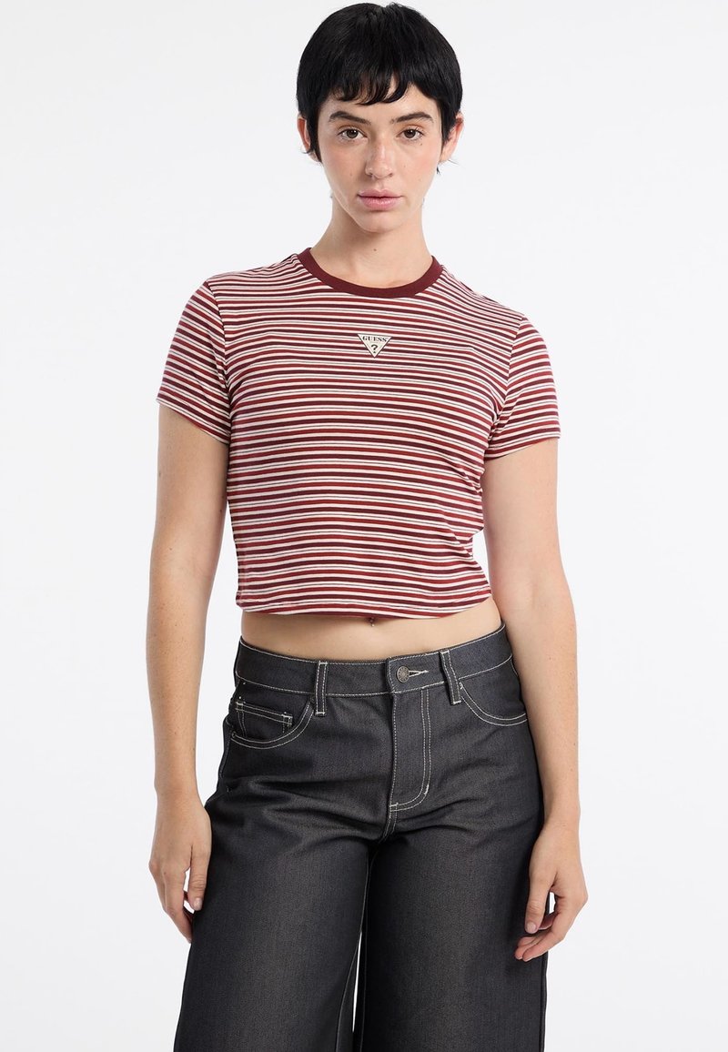 Czerwono-biały, pasiasty crop top z krótkim rękawem i okrągłym dekoltem, ozdobiony trójkątnym logo marki. Połączony z wysokim stanem ciemnych dżinsów.