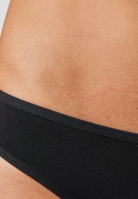 Sous-vêtements en coton noir avec une taille élastique douce, présentant une texture lisse et un minimum de détails de couture le long des bords.
