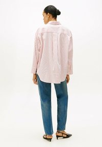 Camisa de manga larga a rayas en rosa y blanco, con cuello, corte relajado y pliegue en la espalda, combinada con jeans rectos azules y zapatos negros.