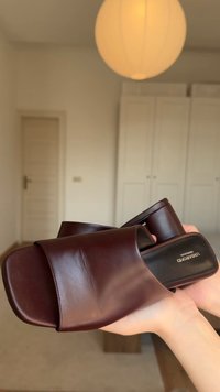 Brūni ādas slides sandales ar atvērtu pirkstu, plakanu zoli un gludu tekstūru. Ievērojams zīmola logotips uz iekšējās zoles un minimālistisks dizains.