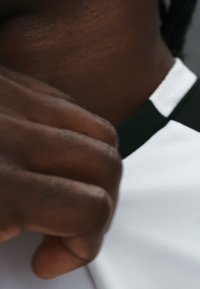 Gros plan d'une main à la peau foncée ajustant le col d'une chemise blanche avec une bordure noire.