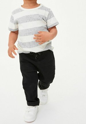 Enfant portant un t-shirt à manches courtes rayé gris et blanc, un pantalon noir à cordon de serrage et des baskets blanches. Tenue simple et décontractée.