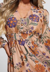 Vestido floral con un suave fondo melocotón, adornado con flores moradas y naranjas. Cintura elástica, mangas largas y diseño de escote en V.