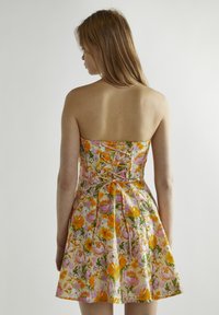 Vestido sin mangas con estampado floral que presenta flores naranjas y rosas sobre un fondo claro, tejido texturizado y un detalle de espalda ajustada.