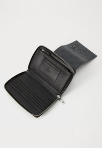 Portefeuille en cuir noir avec une fermeture à glissière. L'intérieur dispose de fentes pour cartes, d'une poche zippée et d'un logo gaufré sur la doublure.