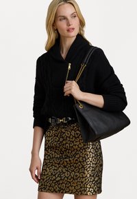 Suéter preto de malha trançada com gola xale, detalhe em zíper dourado; saia mini com padrão de leopardo dourado; bolsa preta com alça de corrente dourada.